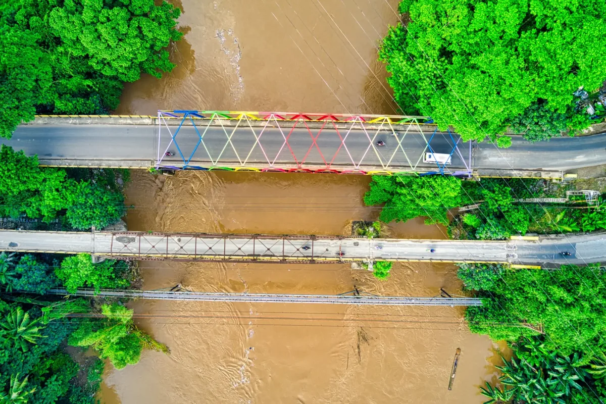 Aerial view of a brown, flooded river under two bridges between green trees